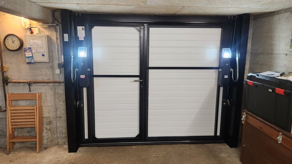 Vue intérieure d’une porte basculante isolée autoportante avec portillon : montants à contrepoids et moteurs embarqués, plafond libre