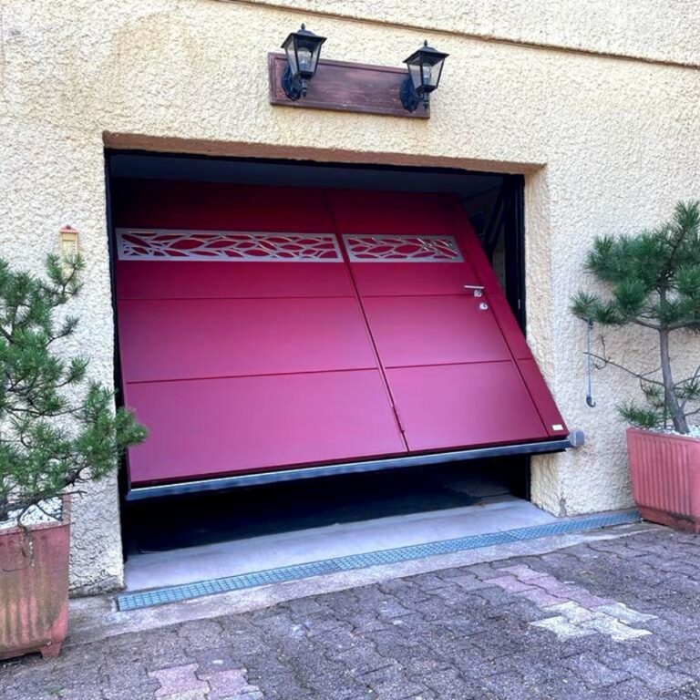 Porte de garage basculante isolée rouge avec portillon et décor ajouré, en cours d’ouverture